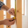 A tape measure showing the standard wall studs distance apart on an unfinished wooden frame.